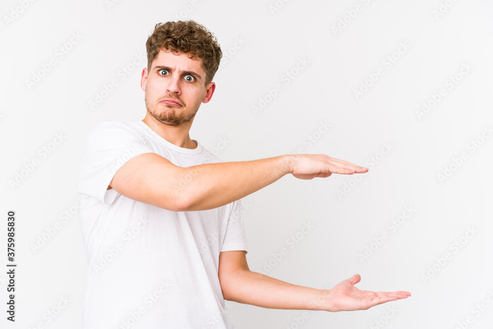 Young blond curly hair caucasian man isolated shocked and amazed holding a copy space between hands. Young blond curly hair caucasian man isolated shocked and amazed holding a copy space between hands.
