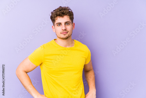 Young blond curly hair caucasian man isolated confident keeping hands on hips. © Asier