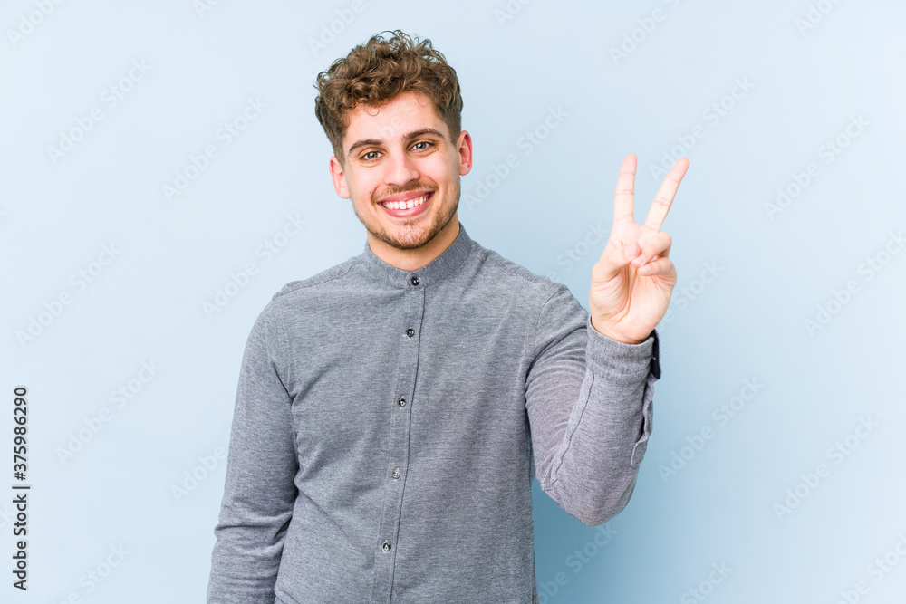 Young blond curly hair caucasian man isolated joyful and carefree showing a peace symbol with fingers. Young blond curly hair caucasian man isolated joyful and carefree showing a peace symbol with fingers.