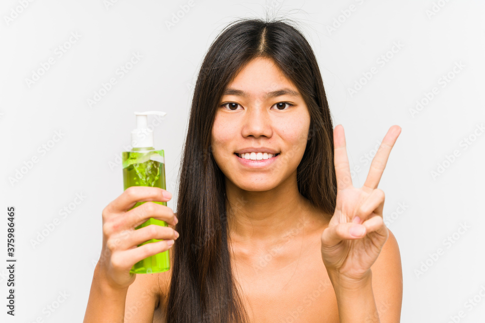 Young chinese woman holding a moisturizer with aloe vera isolated showing number two with fingers. Young chinese woman holding a moisturizer with aloe vera isolated showing number two with fingers.