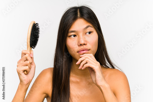 Young chinese woman holding a hairbrush isolated looking sideways with doubtful and skeptical expression.