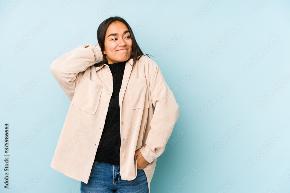 Young woman isolated on a blue background touching back of head, thinking and making a choice. Young woman isolated on a blue background touching back of head, thinking and making a choice.