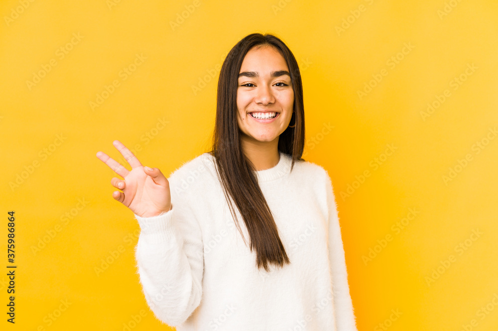 Young woman isolated on a yellow background joyful and carefree showing a peace symbol with fingers. Young woman isolated on a yellow background joyful and carefree showing a peace symbol with fingers.