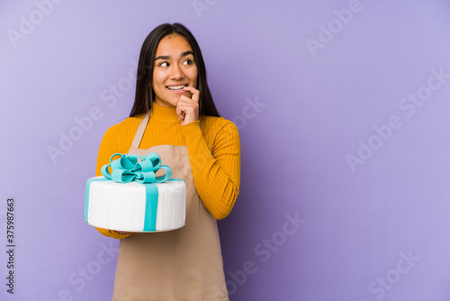 Young asian woman holding a cake isolated relaxed thinking about something looking at a copy space.