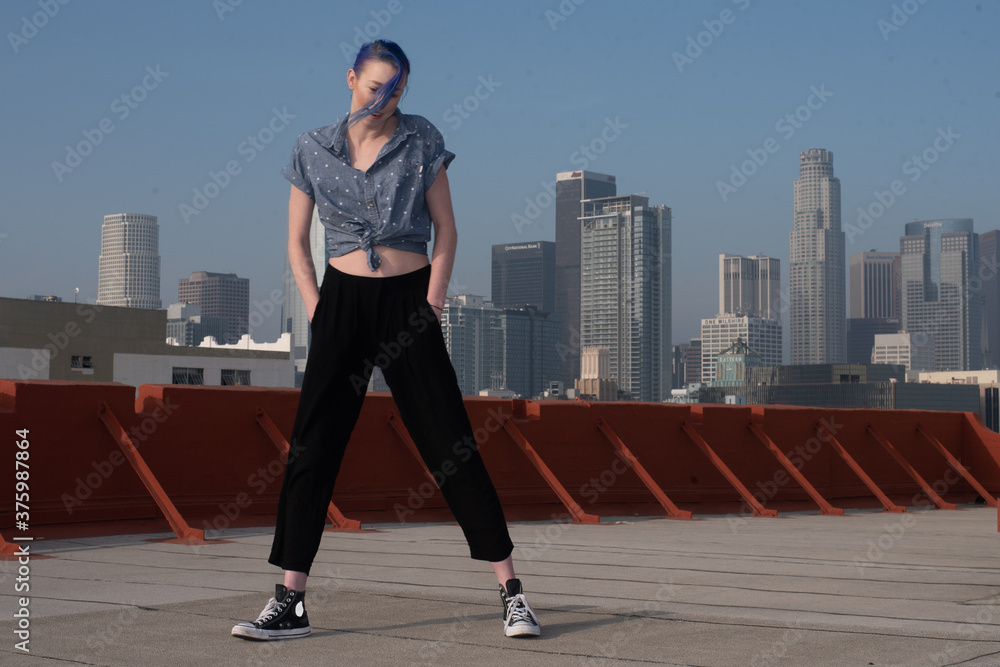 Tall young urban female enjoying the sunshine on a city rooftop overlooking Downtown Los Angeles.