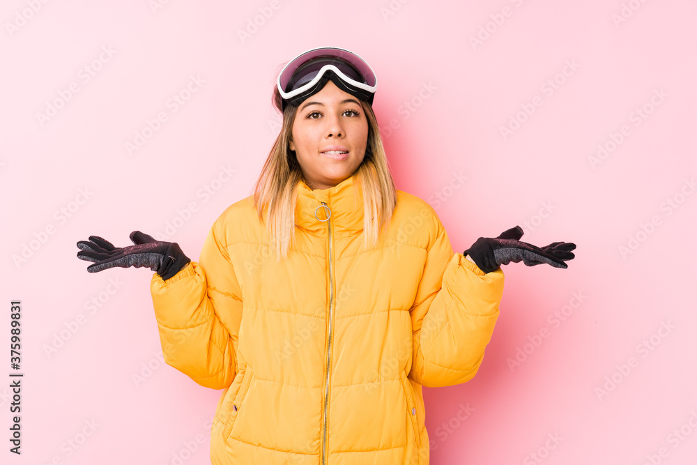 Young caucasian woman wearing a ski clothes in a pink background confused and doubtful shrugging shoulders to hold a copy space. Young caucasian woman wearing a ski clothes in a pink background confused and doubtful shrugging shoulders to hold a copy space.