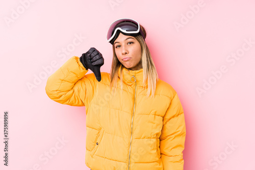 Young caucasian woman wearing a ski clothes in a pink background showing a dislike gesture, thumbs down. Disagreement concept.