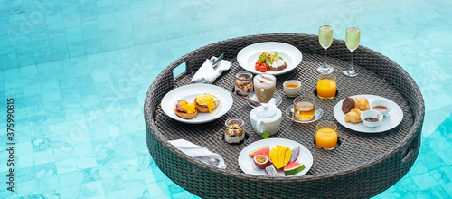 Floating Breakfast tray in swimming pool at luxury hotel or tropical resort villa, fruits; mango, watermelon dragon and passion fruit, food, bread, coffee, tea, wine and orange juice. Exotic summer