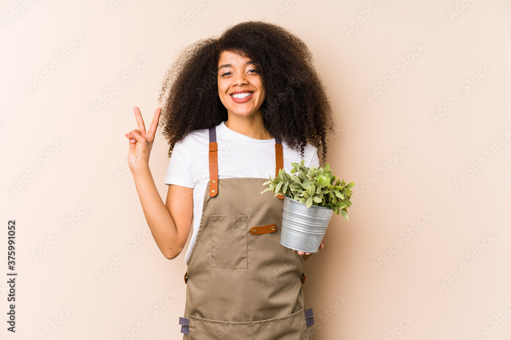Young afro gardener woman holding a plant isolatedshowing number two with fingers. Young afro gardener woman holding a plant isolatedshowing number two with fingers.