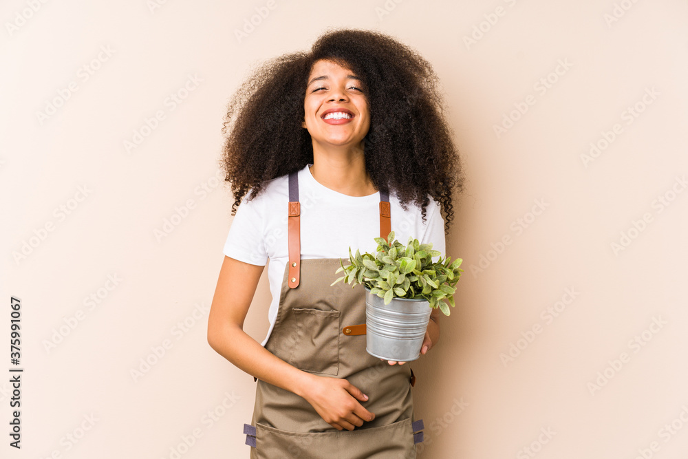 Young afro gardener woman holding a plant isolatedlaughing and having fun. Young afro gardener woman holding a plant isolatedlaughing and having fun.