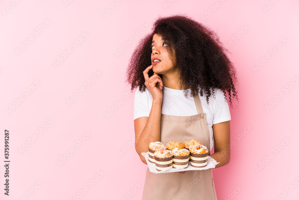 Young afro pastry maker woman holding a cupcakes isolatedYoung afro baker woman relaxed thinking about something looking at a copy space.