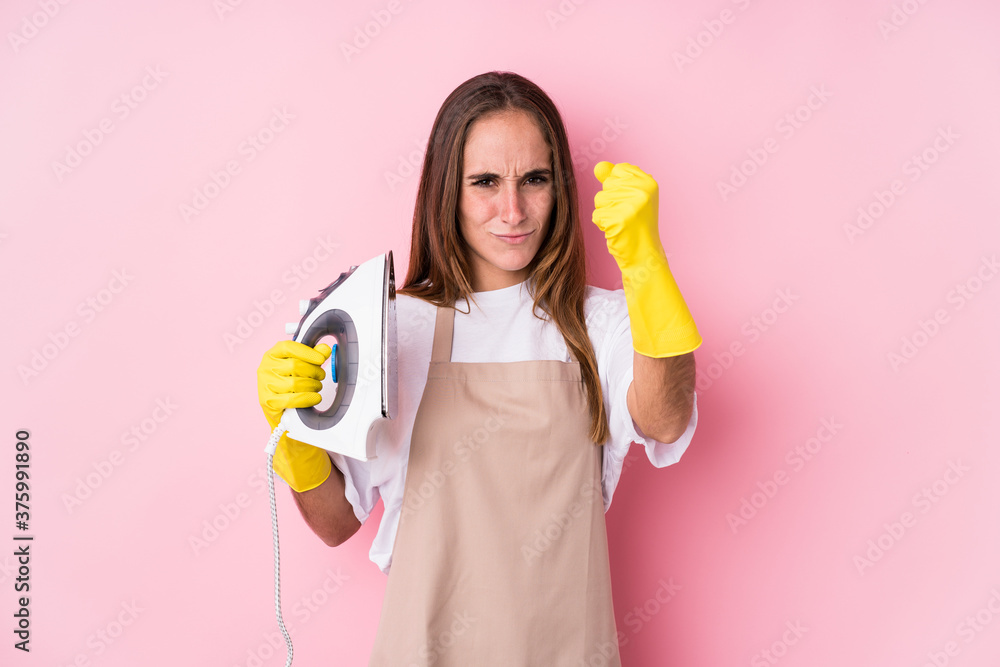 Young caucasian woman with clothes iron isolated showing fist to camera, aggressive facial expression. Young caucasian woman with clothes iron isolated showing fist to camera, aggressive facial expression.