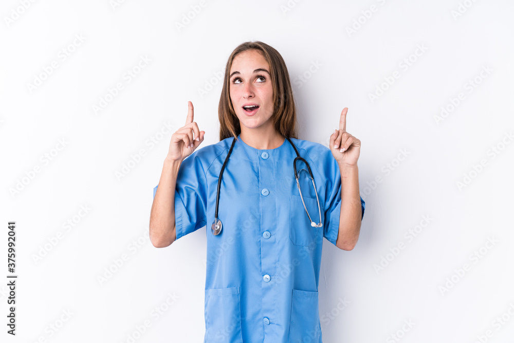 Young nurse woman isolated pointing upside with opened mouth. Young nurse woman isolated pointing upside with opened mouth.