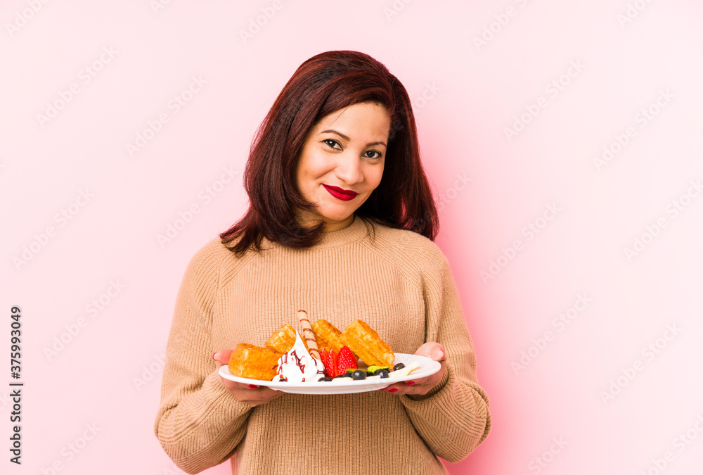 Middle age latin woman holding a waffle isolated happy, smiling and cheerful.