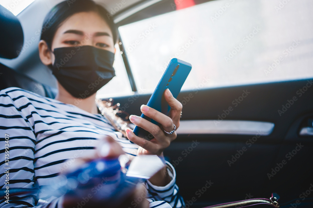 Young asian woman sitting at backseat of car and using mobile and holding credit card in hands.