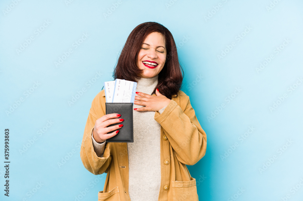 Middle age latin woman holding a passport isolated laughs out loudly keeping hand on chest. Middle age latin woman holding a passport isolated laughs out loudly keeping hand on chest.