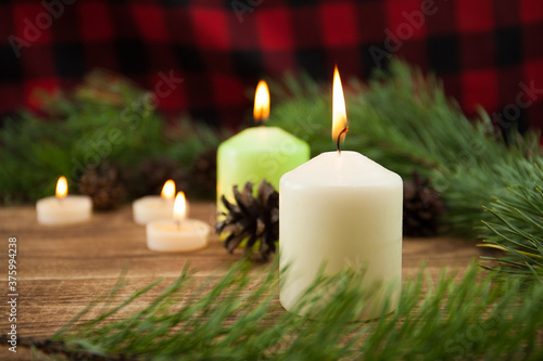 Christmas background  a composition of candles  a blanket  a fir tree  cones and a place for text on a wooden background  focus on the middle plan