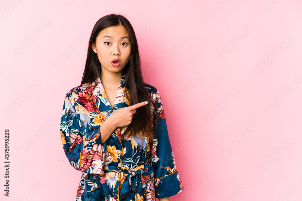 Young chinese woman wearing a kimono pajama isolated pointing to the side Young chinese woman wearing a kimono pajama isolated pointing to the side