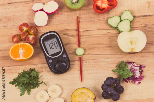 Glucometer with result of sugar level and clock made of fruits with vegetables showing time for dinner