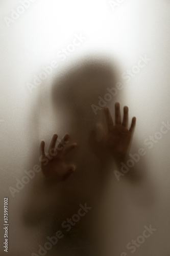 Ghost concept shadow of a child behind the matte glass blurry hand and body soft focus