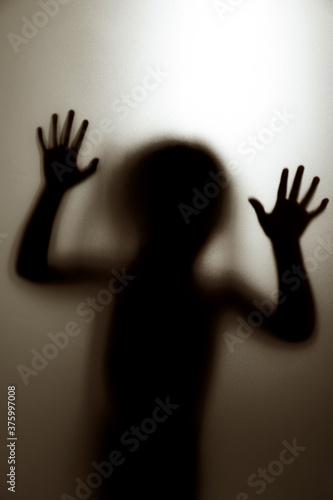 Ghost concept shadow of a child behind the matte glass blurry hand and body soft focus.