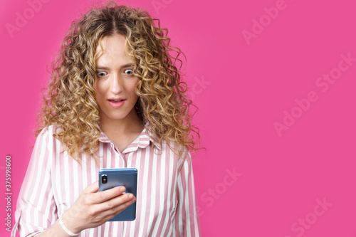 A fashionable woman in a striped shirt, holds a mobile phone, gasps in surprise, reads amazing news.