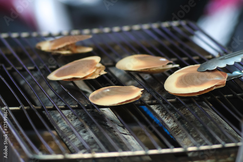 Fresh scallops shells grilling on charcoal rack at Thai market