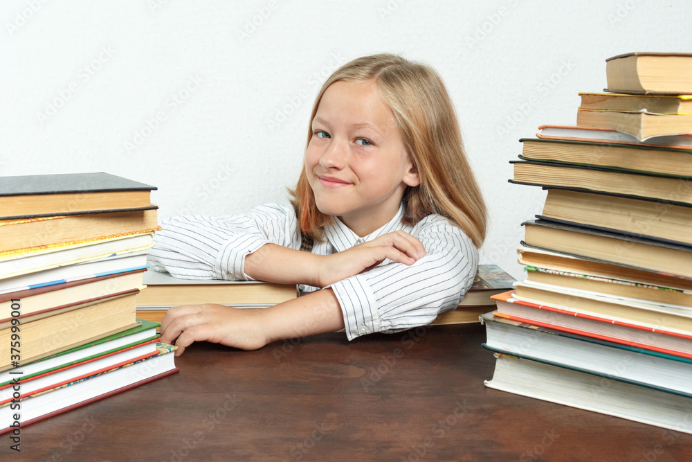 Portrait of a teenage girl who sits at a table among the books. Looks into the camera. Isolated background. Portrait of a teenage girl who sits at a table among the books. Looks into the camera. Isolated background.