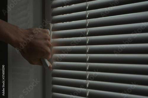 a man opens the white handle of a window with closed blinds