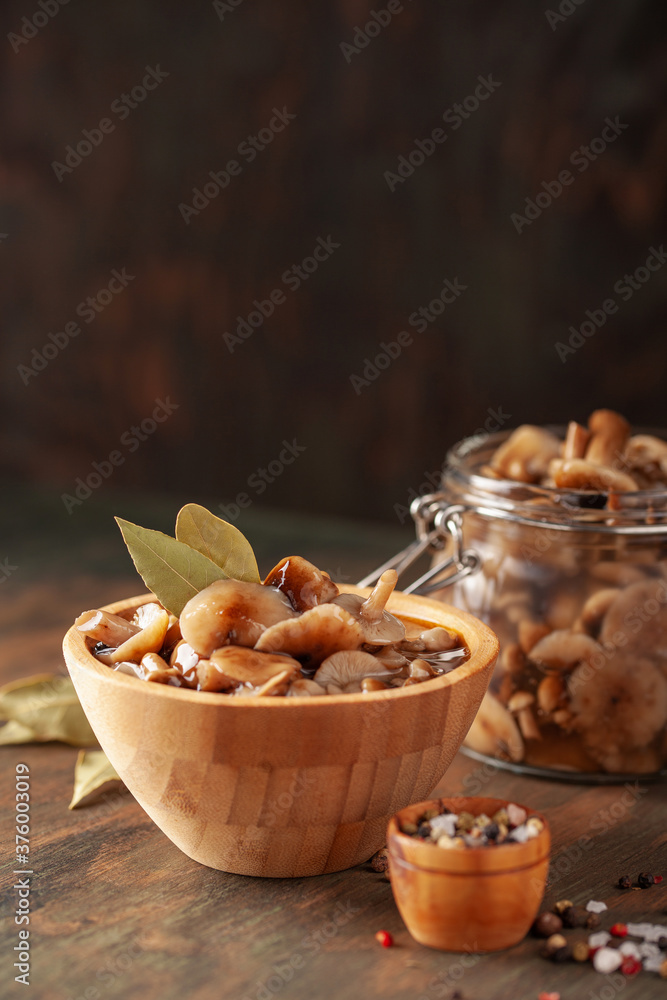 Homemade pickled honey agarics in wooden bowi and  open glass jar, spices, spoon, napkin,  on  wooden table. Marinated mushrooms are valuable source of protein. Fermented healthy food.
