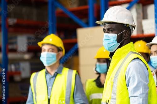 Warehouse worker in protective medical face mask working at large warehouse. Many employees are working intently in the warehouse. Diversity peoples at work.