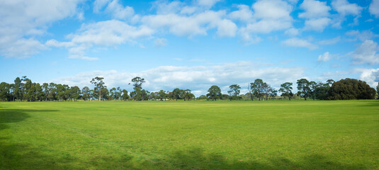 Panoramic view of a large grass field with a well-tended neat lawn against the blue sky. Background texture of grass and trees in a park with vast vacant open space on a sunny day. Copy space for text