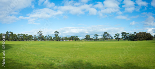 Panoramic view of a large grass field with a well-tended neat lawn against the blue sky. Background texture of grass and trees in a park with vast vacant open space on a sunny day. Copy space for text