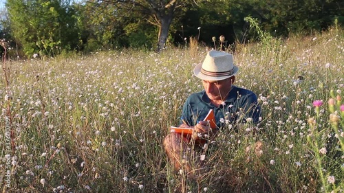 Middle Age Man Sitting in Grass and Writing in His Notebook