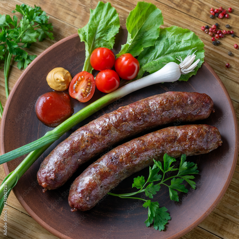 Food poster, restaurant setting - a portion of grilled sausages with tomatoes and herbs, ketchup, mustard. On a rustic table. Food poster, restaurant setting - a portion of grilled sausages with tomatoes and herbs, ketchup, mustard. On a rustic table.