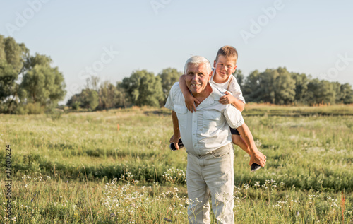 Happy child with Grandfather playing at the meadow. Grandpa retiree. Retirement parent