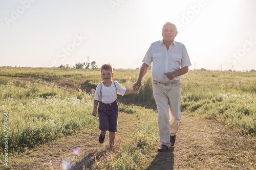 Happy child with Grandfather playing at the meadow. Grandpa retiree. Retirement parent