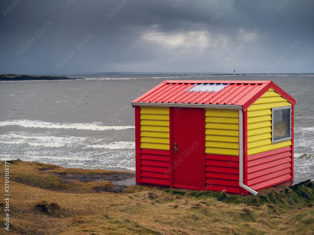 Vivid red and yellow lifeguard house overlooking ocean. Nobody. Rosses point beach county Sligo, Ireland. Dramatic cloudy sky. Vivid red and yellow lifeguard house overlooking ocean. Nobody. Rosses point beach county Sligo, Ireland. Dramatic cloudy sky.