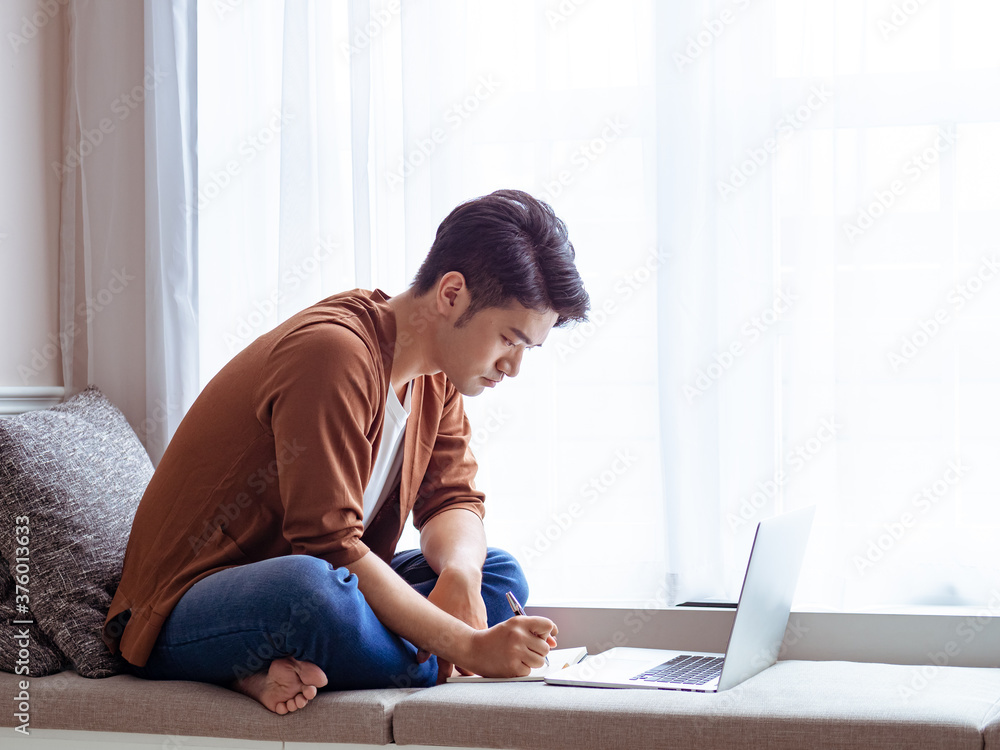 Young asian man writing in notebook and using laptop. Young asian man writing in notebook and using laptop.