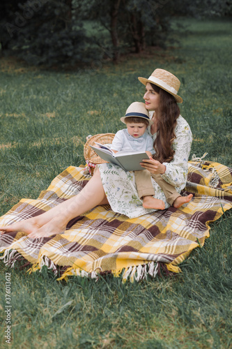 Family picnic in the park. Mother with her little pretty son sitting on blanket and reading book.