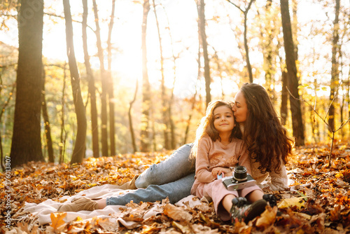 Stylish young Mother and daughter walking in the autumn forest at sunset. Mother and daughter embrace in autumn park. Mom and child having fun together in autumn. Family on a walk. 