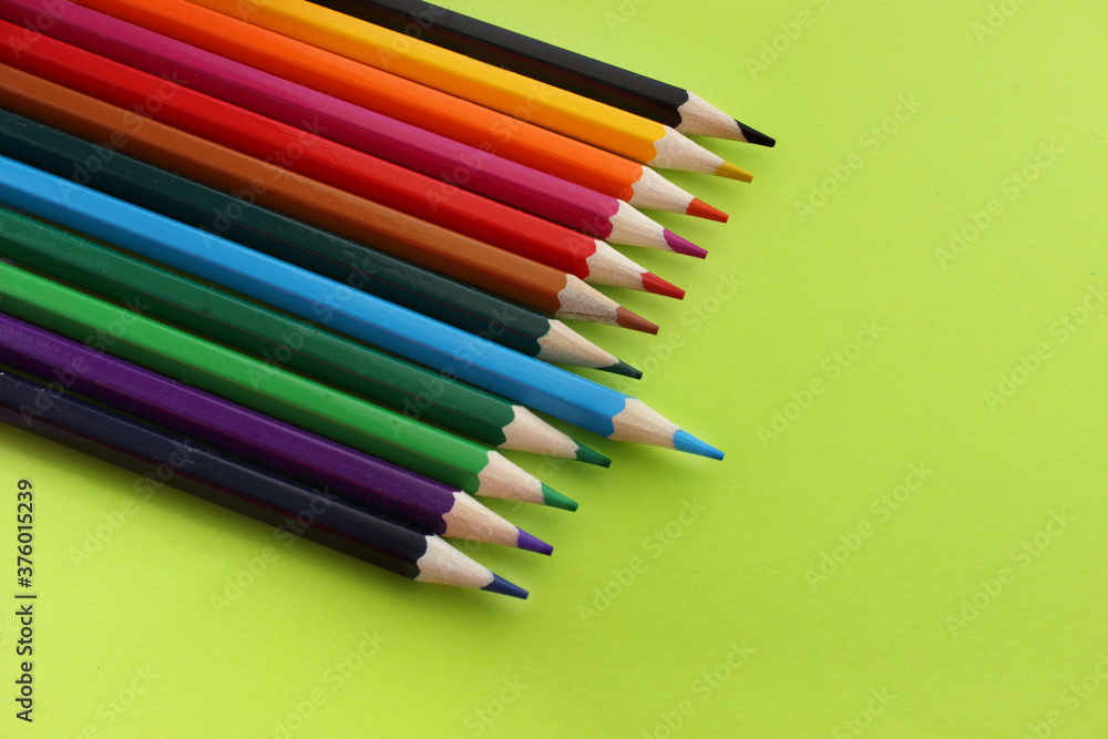 Colored pencils on yellow background. Lots of different colored pencils. Pencils are very sharp. Pencils lie in top corner. Blue pencil is pushed forward. Close-up. Copy space. Background. Flat lay Colored pencils on yellow background. Lots of different colored pencils. Pencils are very sharp. Pencils lie in top corner. Blue pencil is pushed forward. Close-up. Copy space. Background. Flat lay