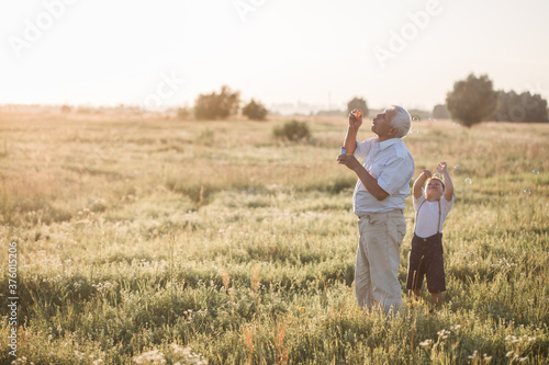 Happy senior man Grandfather with cute little boy grandson playing in field. Happy child with Grandfather playing outdoors