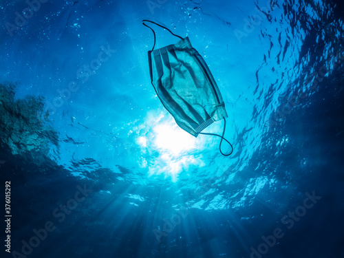 Concept of ocean pollution with a used one way facemask floating under water