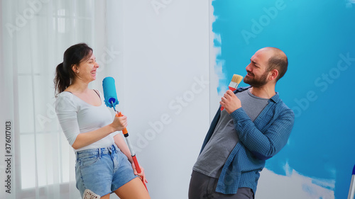 Couple full of happiness while giving their apartment a renovation. Singing on roller brush. Home decoration and renovation in cozy apartment flat, repair and makeover