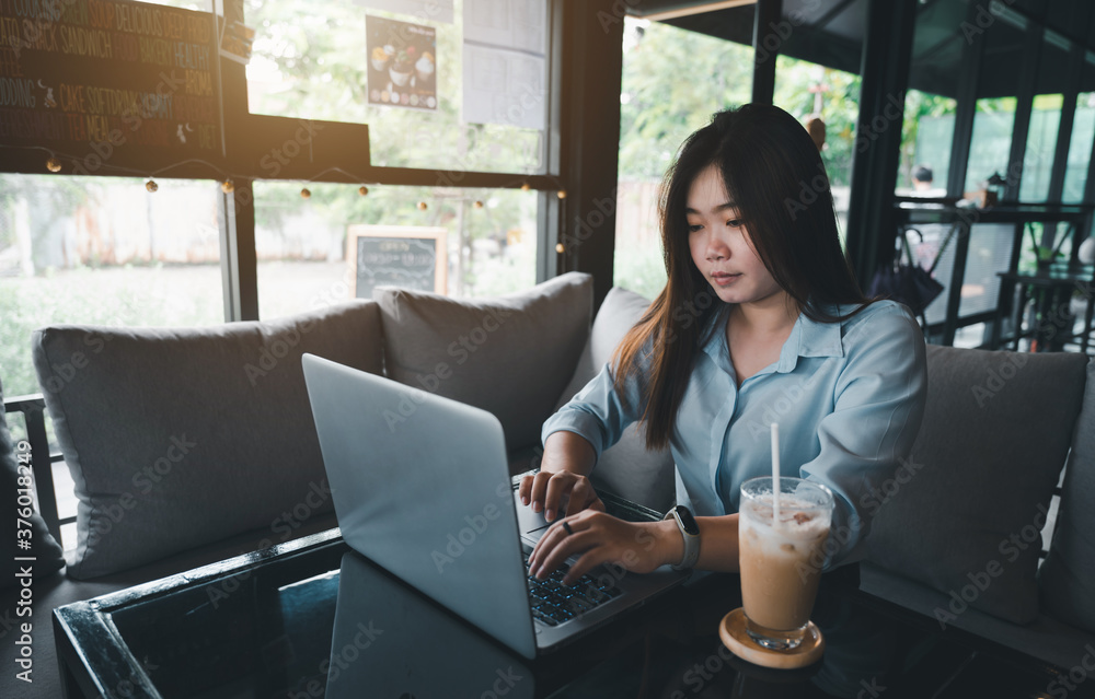 A female Asian office worker of Thai descent is typing and working with notebooks in a coffee shop during the day. She was wearing a blue shirt and sipping coffee. A female Asian office worker of Thai descent is typing and working with notebooks in a coffee shop during the day. She was wearing a blue shirt and sipping coffee.