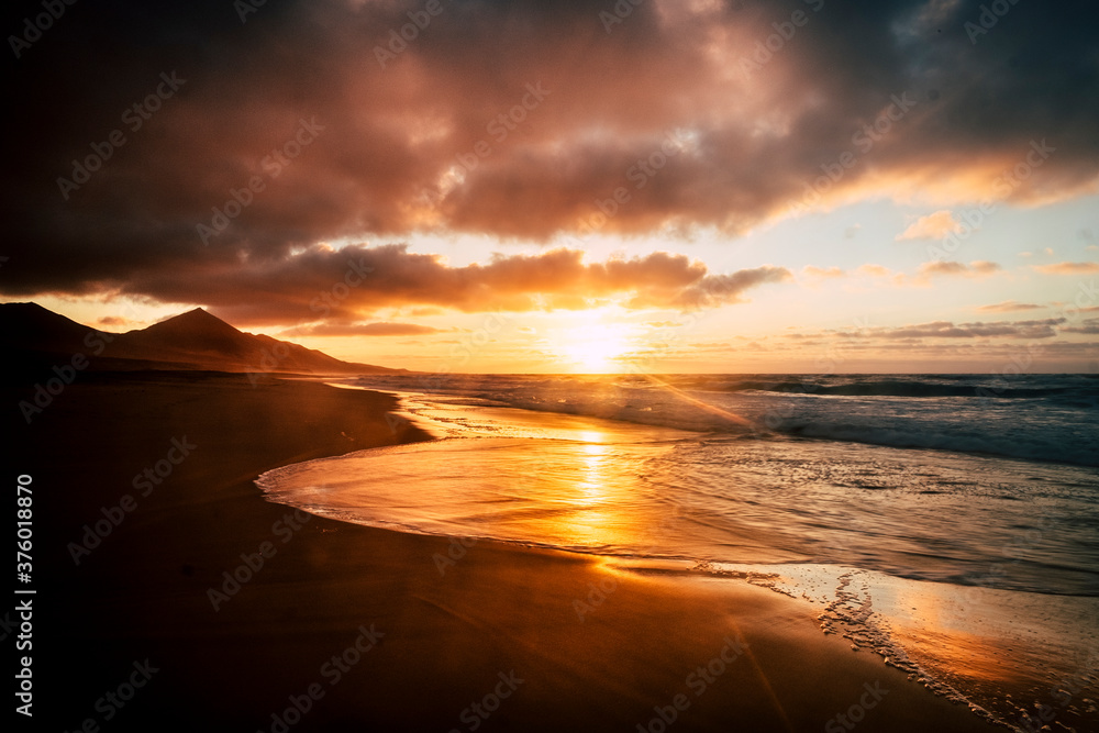 Wonderful timeless sunset at the beach with dramatic clouds and waves - mountains in background and wild scenic place - golden and fire colors in a beauty of nature