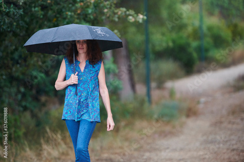 woman walking in the rain with black umbrella in rural setting © Francisco