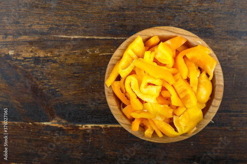 Sliced raw yellow peppers in a bowl on a wooden background. Vegetable, ingredient and staple food.