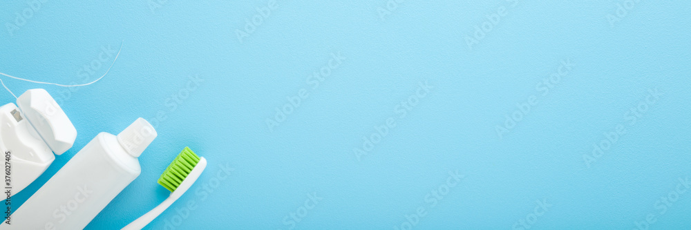 White tube of toothpaste, toothbrush with green bristles and container of dental floss on pastel light blue background. People teeth hygiene. Empty place for text or logo. Wide banner. Top down view. White tube of toothpaste, toothbrush with green bristles and container of dental floss on pastel light blue background. People teeth hygiene. Empty place for text or logo. Wide banner. Top down view.